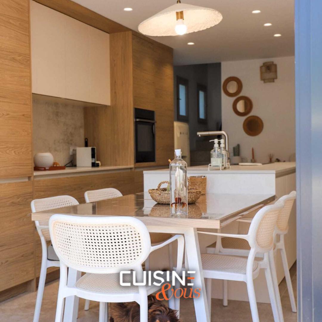Cuisine design à Nîmes, réalisée sur mesure par Cuisine & Vous, avec meubles en bois clair et blanc, îlot central fonctionnel et table contemporaine pour une ambiance chaleureuse.