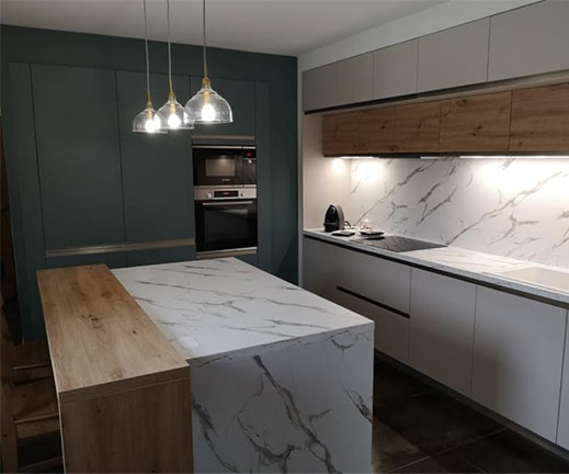 Cuisine moderne avec îlot central en stratifié marbre, façades bleu profond et cachemire, et éclairage suspendu en verre.